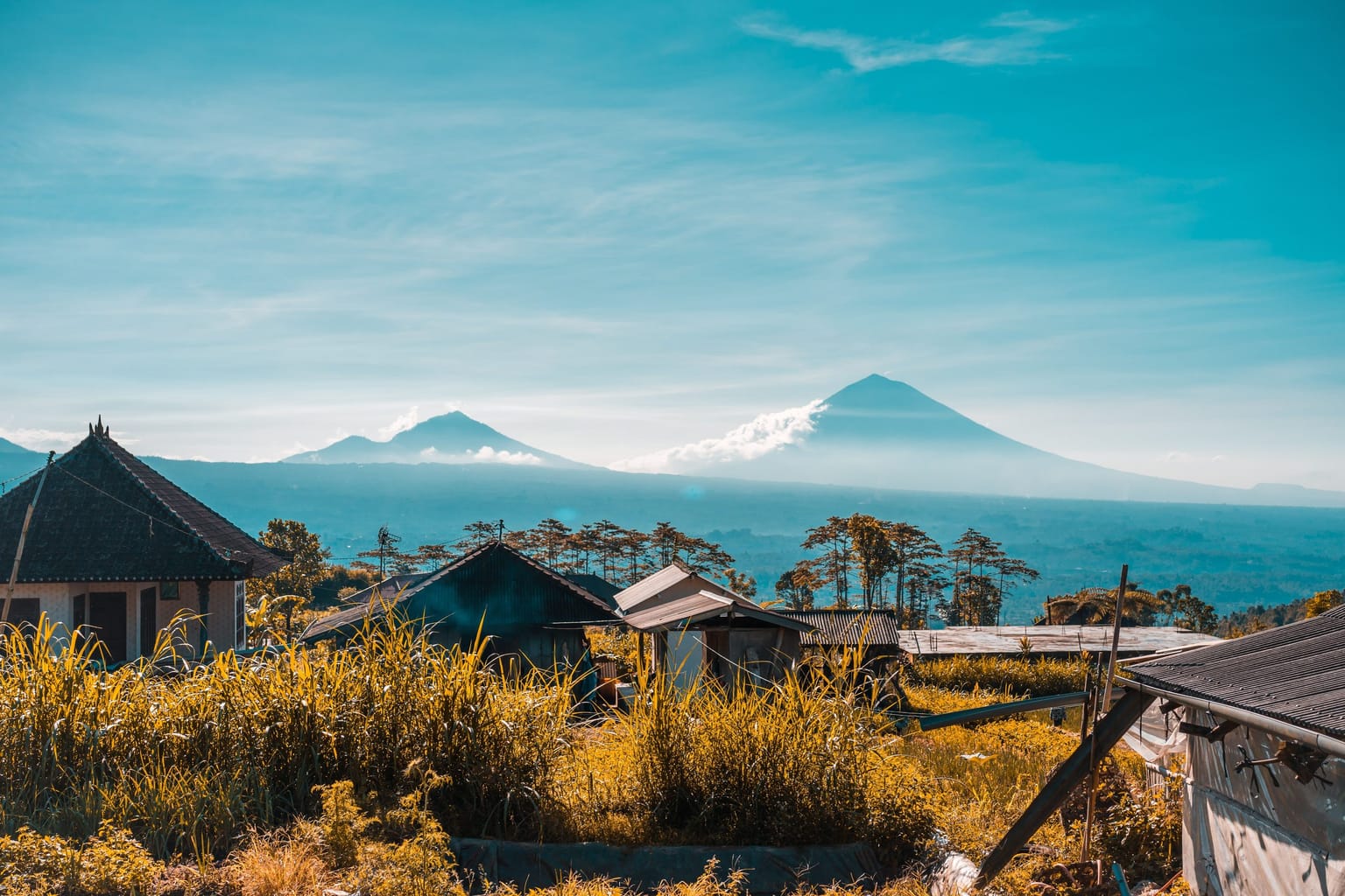 A mountain village with traditional roofs beneath a distant volcano.