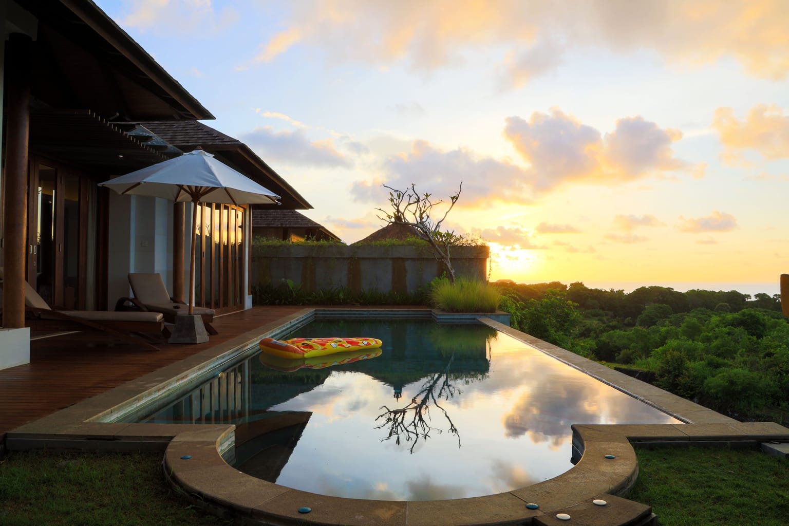 A villa pool and loungers at sunset with the ocean in the distance.